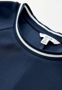 Granatowy sweatshirt z prążkowanym dekoltem w okrągłym kształcie, zdobiony białymi paskami. Miękka faktura z metką wskazującą markę i rozmiar.
