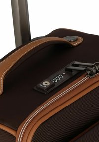 Valigia di stoffa marrone con superficie texturizzata, dettagli in pelle marrone, un lucchetto combinato e cuciture bianche a contrasto lungo la cerniera.