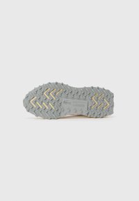 Grijze rubberen buitenzool met een zigzagloopprofiel en gele accenten. Bevat reliëflogo-details; ontworpen voor grip en stabiliteit.