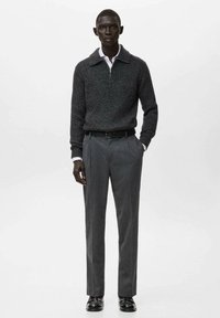 Szary pulower z dzianiny z kołnierzem, noszony na białej koszuli zapinanej na guziki, w połączeniu z szarymi dopasowanymi spodniami i czarnymi butami.