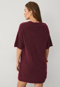Bordeaux oversized strikkjole med korte ærmer, rund halsudskæring og en blød tekstur. Har en afslappet pasform og subtile detajler i kanten.