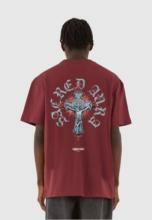 Mørkerød kortærmet t-shirt med et grafisk motiv af et kors med en figur og udsmykkede detaljer i blå og rød, med teksten "Sacred Army".