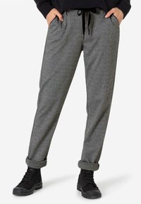 Grau gemusterte Hosen im Fischgrätmuster mit lockerer Passform, ausgestattet mit einem Bund mit Kordelzug, seitlichen Taschen und umgenähten Säumen, kombiniert mit schwarzen Stiefeln.