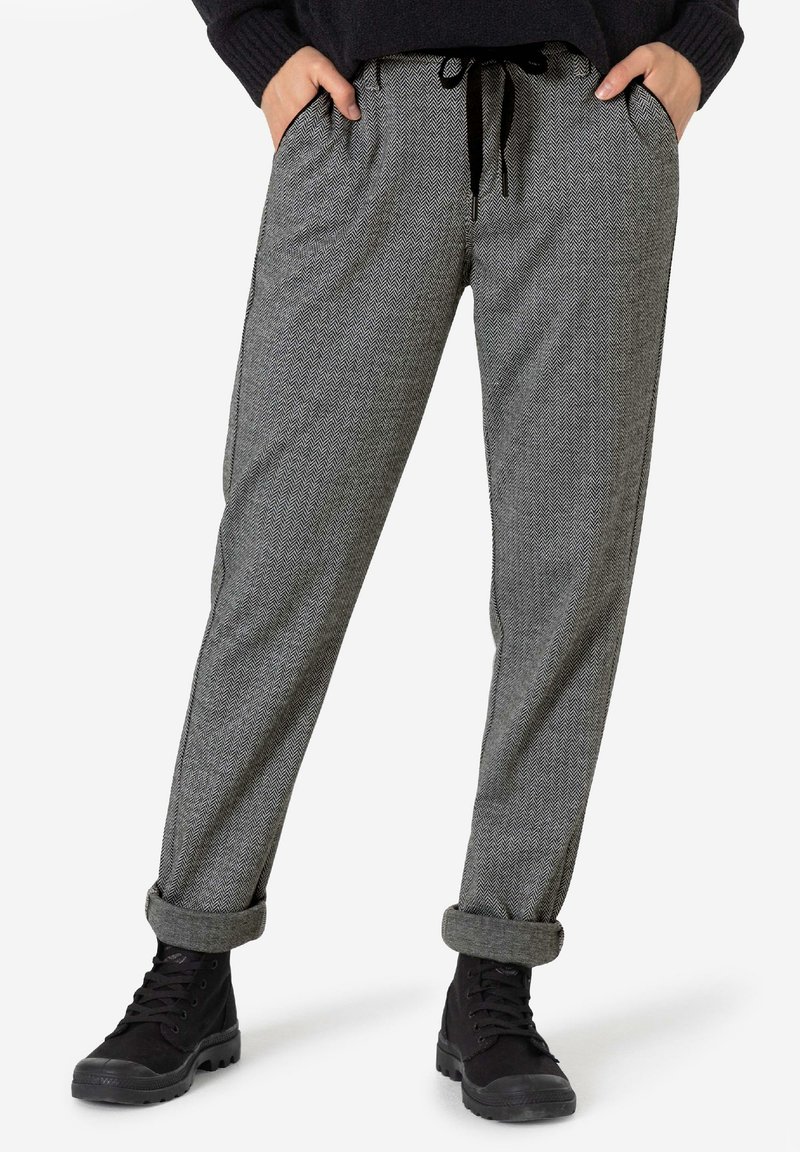 Grau gemusterte Hosen im Fischgrätmuster mit lockerer Passform, ausgestattet mit einem Bund mit Kordelzug, seitlichen Taschen und umgenähten Säumen, kombiniert mit schwarzen Stiefeln.
