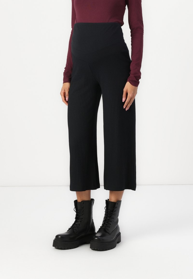 Culottes negros acanalados con cintura alta, combinados con botas negras hasta el tobillo con cordones. La parte superior es de manga larga color granate. Texturas suaves en todo el conjunto.