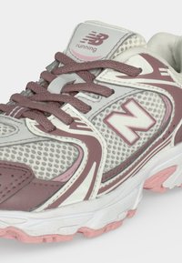 Λευκό και ροζ παπούτσι τρεξίματος New Balance με πάνω μέρος από δίχτυ και συνθετικό υλικό, που διαθέτει ροζ κορδόνια και μαλακή σόλα.