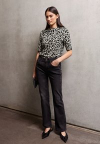 Bežovo-černý top s leopardím potiskem a krátkým rukávem, v kombinaci s černými džínami s vysokým pasem a černými špičatými botami. Jednoduchá kabelka s cvočky.