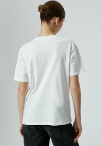 Hvid bomulds t-shirt med korte ærmer og rund halsudskæring, med en afslappet pasform og syet kant. Bagview viser minimal udsmykning.