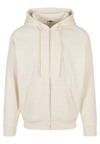 Sudadera cremosa con cremallera y cordones, bolsillos frontales, puños y dobladillo acanalados. Fabricada con tejido suave, presenta un corte relajado y mangas raglán.