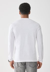 Langes weißes T-Shirt aus Baumwolle mit Rundhalsausschnitt, schlichter Textur und lässigem Schnitt, kombiniert mit grauen, verwaschenen Jeans.
