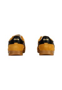 Baskets en daim jaunes avec accents noirs, présentant une finition texturée et une semelle en caoutchouc. Logo "Gola" affiché en évidence sur le talon.