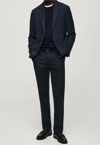 Marynarka w kolorze granatowym wykonana z teksturowanej tkaniny, zestawiona z ciemnym swetrem i dopasowanymi spodniami. Całość uzupełniona czarnymi skórzanymi butami i cienkim paskiem.