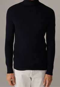 Maglione a collo alto in maglia a coste di colore blu navy, con maniche lunghe, design aderente e dettagli sottili sulle spalle. Texture morbida e tonalità uniforme.