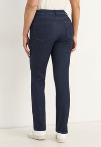 Mörkblå denimbyxor med slim fit, med två bakfickor och en strukturerad midja. Bärs med vita sneakers.