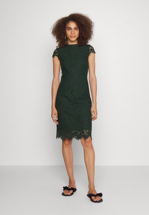 Tamsiai žalia nertinė suknelė su trumpomis rankovėmis ir banguotu kraštu. Turi prigludusį siluetą, gėlių raštus ir sudėtingus išsidižius. Dėvima su juodais šlepetėmis.