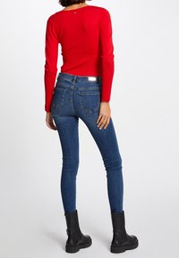 Punainen istuva pitkähihainen paita yhdistettynä tummansinisiin skinny-farkkuihin, joissa on klassinen viiden taskun muotoilu, sekä mustat nilkkasaappaat.