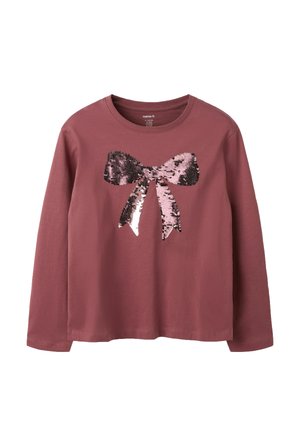 Chemise mauve à manches longues avec col rond et un grand nœud rose et noir pailleté sur le devant.