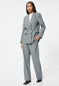 Blazer gris de doble botonadura con un acabado texturizado, combinado con pantalones a medida a juego. El modelo lleva una blusa blanca y botas negras.