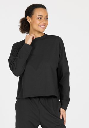 Schwarzes Sweatshirt mit lockerer Passform, langen Ärmeln und hohem Kragen. Aus weichem Material gefertigt, mit minimaler Nahtführung und kürzerem Design.