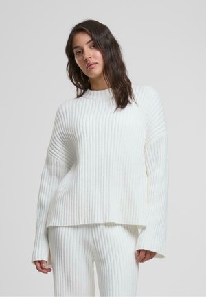 Pull en maille côtelée blanc avec des manches longues, décolleté large et coupe décontractée, associé à un pantalon côtelé assorti. Texture douce, design minimal.