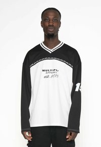 Schwarz-weiße Langarmshirt mit V-Ausschnitt, Aufdruck "MULTIPLY APPAREL est. 2015" und seitlichen Streifenakzenten. Nummer 15 am Ärmel.