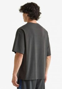 Maglietta grigia scura a maniche corte con collo a giro, realizzata in morbido cotone, caratterizzata da una vestibilità rilassata e dettagli di cucitura minimalisti all'orlo.