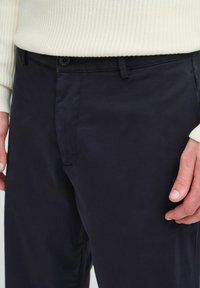 Navy trousers with a flat front and subtle texture, featuring a button closure and side pockets, paired with a cream ribbed sweater.