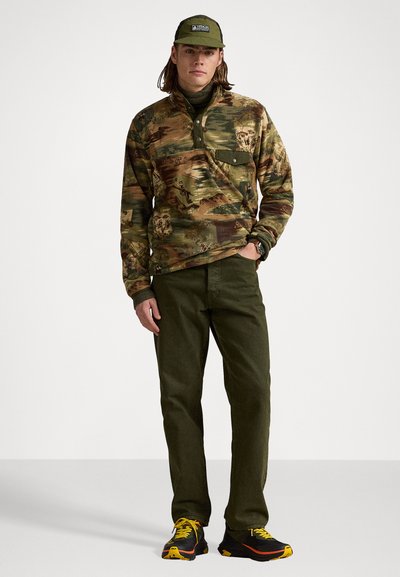 Camo-patterned pullover shirt with a buttoned placket, paired with olive-green pants and black sneakers with yellow accents and textured soles.
