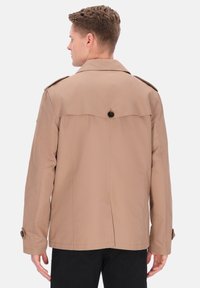 Beige jakke lavet af letvægtsstof, med klassisk krave, knaplukning ved ærmerne og bageste sømdetalje for en struktureret pasform.