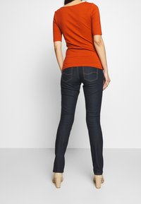 Pomarańczowa dopasowana bluzka z krótkim rękawem, zestawiona z ciemnoniebieskimi, obcisłymi dżinsami z przeszyciami na tylnej kieszeni i lekkim postarzeniem.