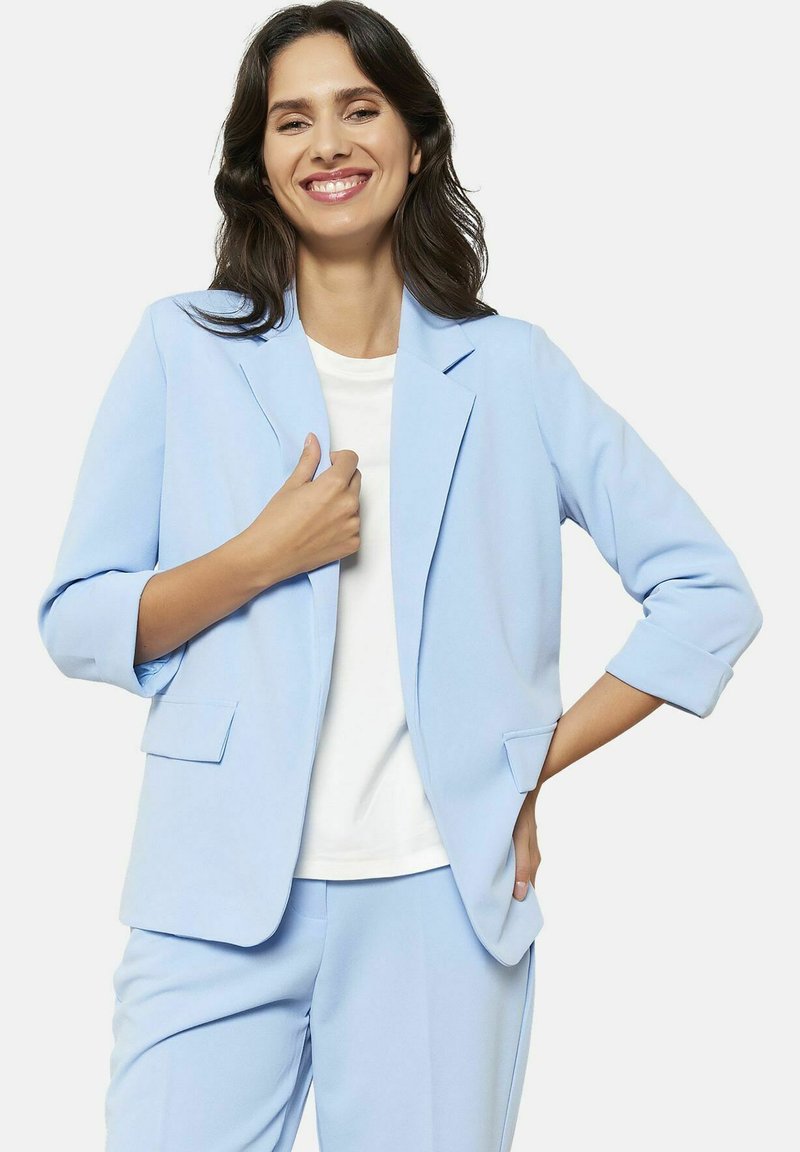 Blazer azul claro hecho de tela suave, con un solo botón, solapas tipo muesca y dos bolsillos frontales, combinado con una blusa blanca.