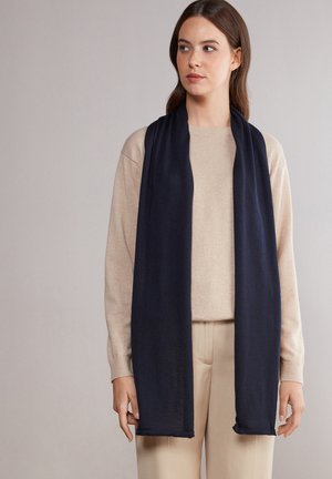 Marineblauwe sjaal, lang en slank, gemaakt van zachte stof met een gladde textuur. Heeft ruwe randen en hangt elegant om de hals.