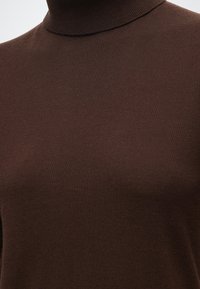 Gros plan d'un pull à col roulé marron en laine, montrant la texture du tissu et les détails de l'encolure.