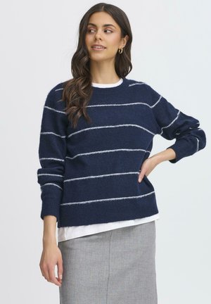 Marineblå stribet sweater med hvide vandrette striber, lavet af et blødt materiale, med rund halsudskæring og afslappet pasform, båret over en hvid skjorte.