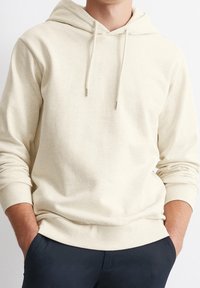 Felpa color beige chiaro realizzata in morbido tessuto in cotone misto. Presenta una tasca a canguro, cappuccio con coulisse e polsini e orlo a coste.