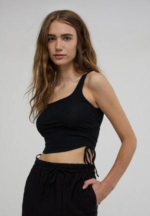 Top crop nero a coste con una spalla e lati arricciati; tessuto testurizzato. Abbinato a pantaloni neri a vita alta con coulisse.