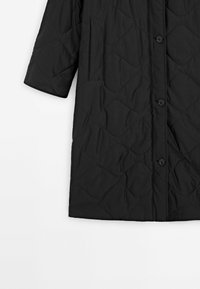 Manteau matelassé noir avec manches longues, boutons au devant, et poches fendues sur les côtés.