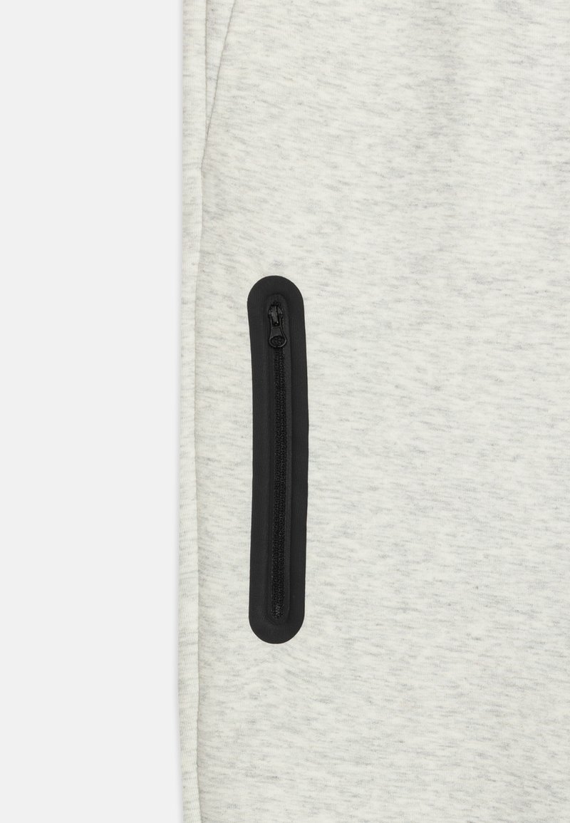 Pantalons de survêtement gris clair avec une coupe slim, une texture douce et une poche zippée noire sur le côté pour un rangement sécurisé.