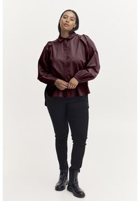 Burgundy, long-sleeved shirt with a high collar and gathered shoulders; paired with black fitted pants and black ankle boots.