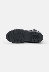 Semelle de chaussure en caoutchouc noir avec un motif de relief, présentant de profonds rainurages et crêtes pour une meilleure traction. Le design est robuste et fonctionnel.
