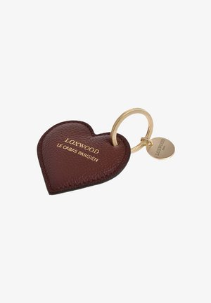 Porte-clés en cuir bordeaux foncé en forme de cœur avec logo doré en relief, attaché à un anneau en métal doré et une étiquette de pendentif. Texture lisse.