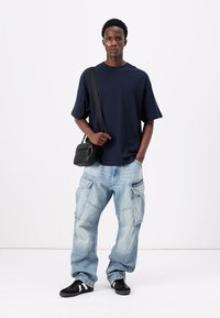 Tricou bleumarin cu mâneci scurte, blugi cargo de culoare albastru deschis cu buzunare, geantă de umăr neagră și teniși negri cu dungi albe.