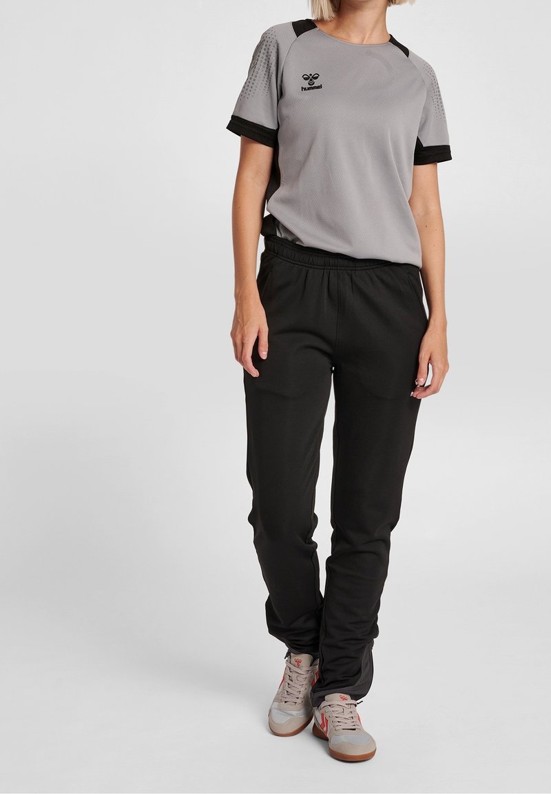 Harmaa urheilupaita mustilla yksityiskohdilla ja lyhyillä, teksturoiduilla hihoilla, yhdistettynä kapeisiin mustiin treenihousuihin ja harmaisiin lenkkareihin.