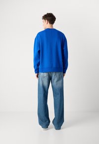 Sweatshirt azul oversized com um decote redondo e um detalhe de costura vertical, combinado com jeans de corte largo azul claro e calçado branco.