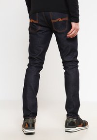 Mörkblå jeans med ljusorange sömmar, slim fit-design, med två bakfickor och en subtil präglad logotyp. Bärs med sportiga sneakers.