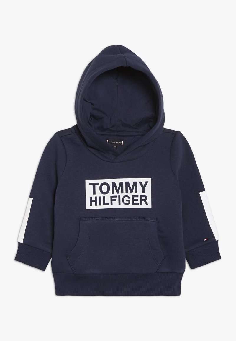 Sudadera con capucha azul marino con un gran logo blanco "TOMMY HILFIGER", bolsillo canguro frontal y detalles blancos en las mangas. Material de algodón.