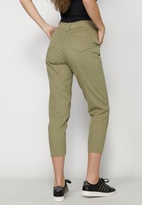Pantalones verde oliva, ajustados y con cintura elástica, dos bolsillo traseros y una textura suave y lisa. Combinados con zapatillas negras.