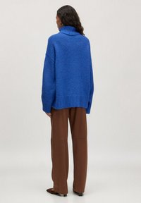 Übergroßer blauer Strickpullover mit hohem Kragen, geripptem Saum, überschnittenen Schultern und weichem Material, kombiniert mit braunen weiten Hosen.