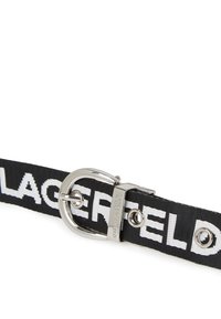 Cinturón de tela negra con grandes letras blancas. Presenta una hebilla de metal plateado brillante y remaches, con una textura tejida en toda su superficie.