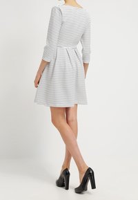Biała sukienka w czarne poziome paski, z rękawami do łokci, dopasowanym korpusem i rozkloszowanym dołem. Nosi się z czarnymi szpilkami.